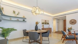 Een moderne eetruimte met een ronde houten tafel, grijze gestoffeerde stoelen en een hangende lamp.
