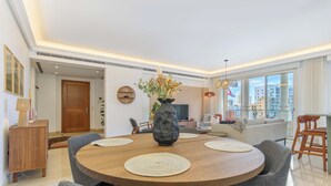 Een moderne eethoek met een ronde houten tafel, grijs gestoffeerde stoelen en een vaas met bloemen.