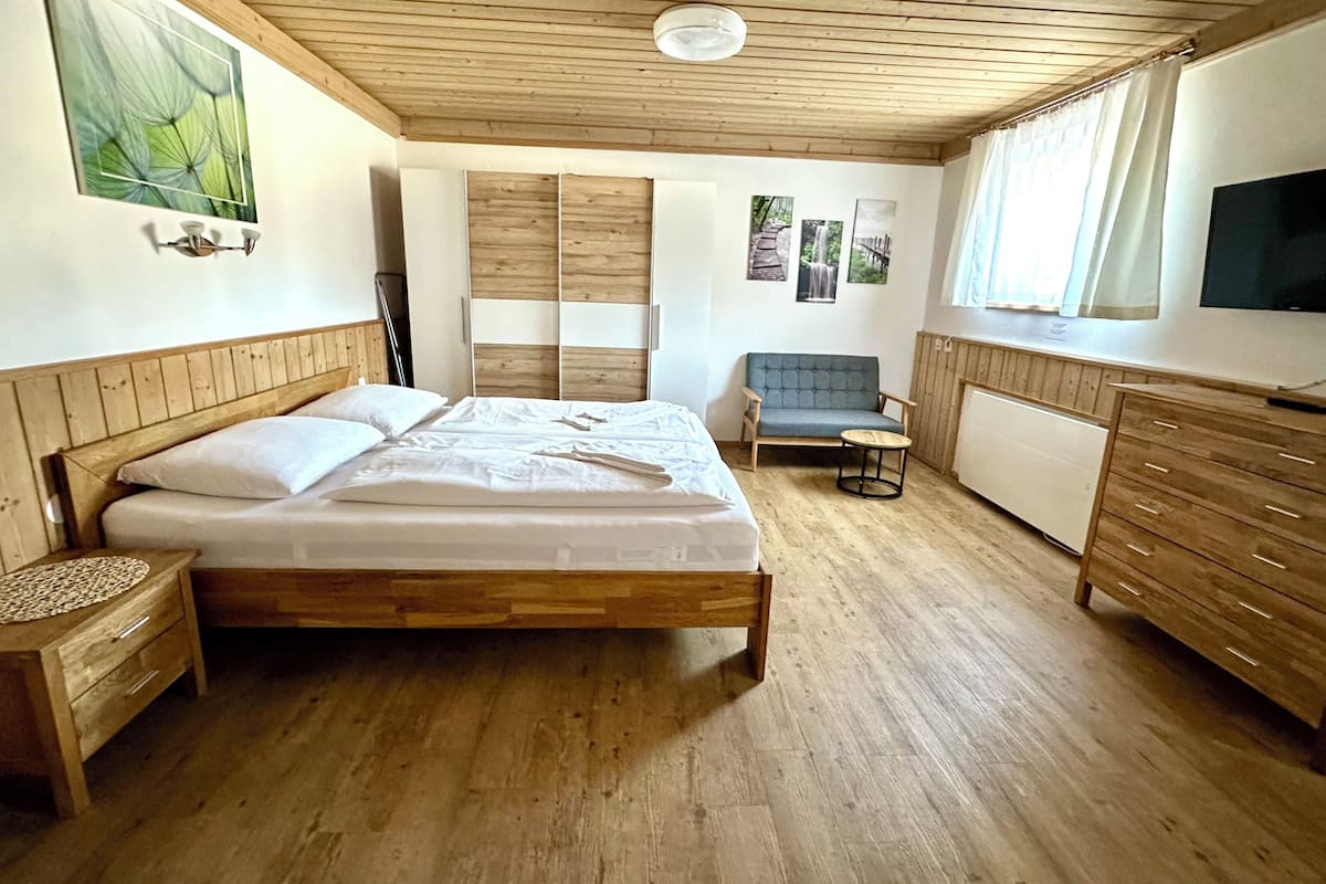 A bedroom with a wooden bed, a small table, a chair, a TV, and a radiator.
