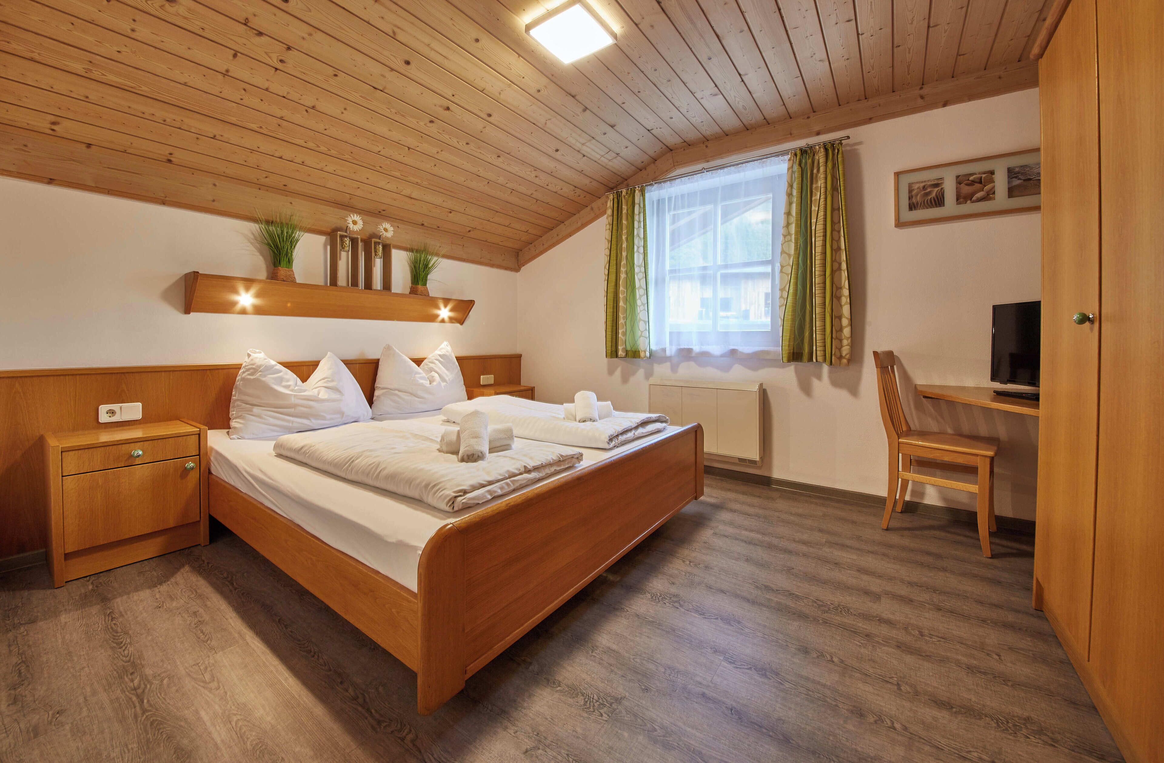 Quarto com cama de madeira, mesa de cabeceira e escrivaninha com cadeira.