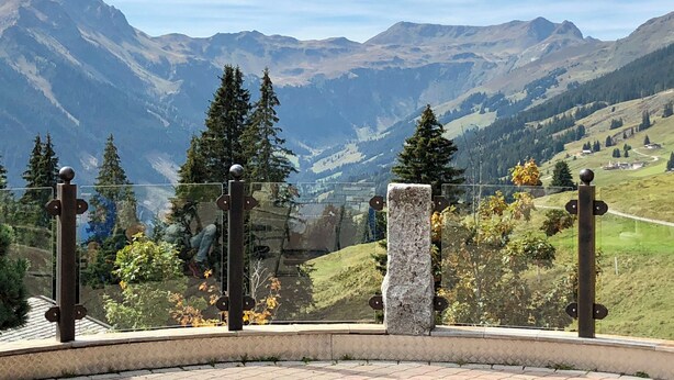 Vista de la montaña desde un balcón con un pilar de piedra y barandilla de metal.