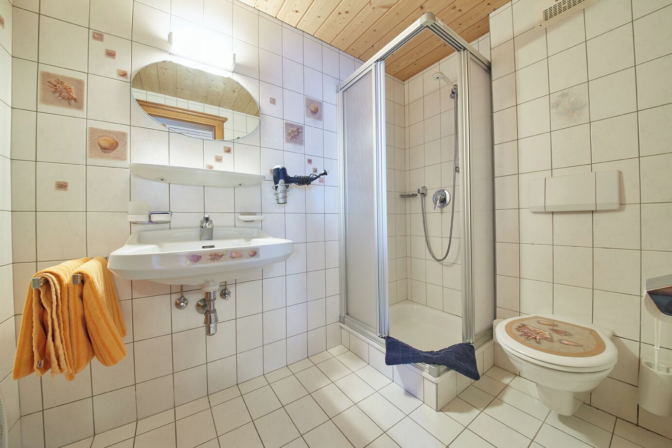 Egy fürdőszoba, amelyben mosdókagyló, tükör, zuhanyzó és WC található.
