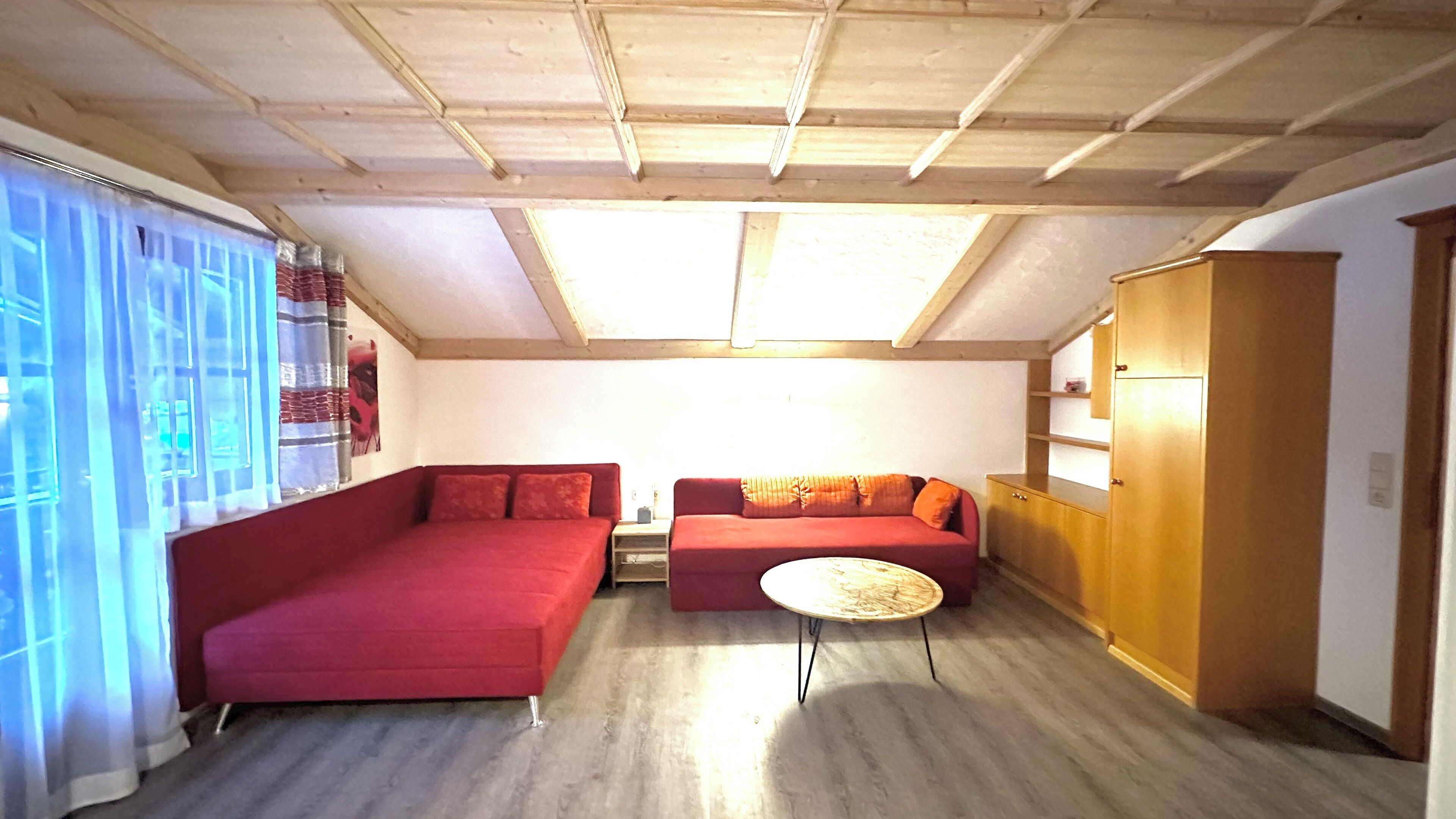 A room with a red sofa, a smaller red couch, a round table, and a wooden cabinet.