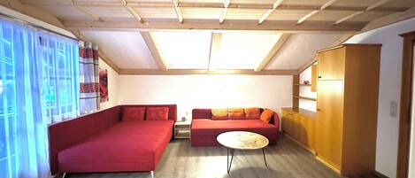 A room with a red sofa, a smaller red couch, a round table, and a wooden cabinet.