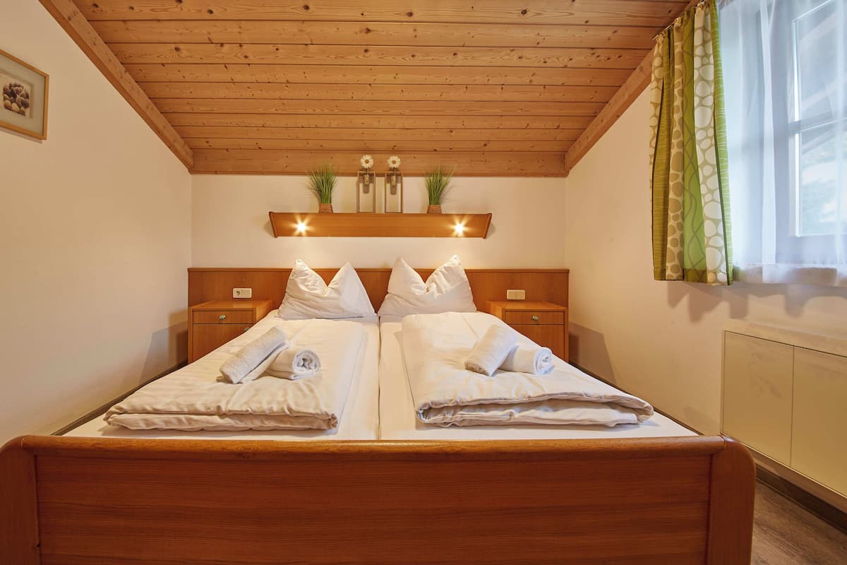 A double bed with white linens, wooden headboard, bedside tables, and a wooden ceiling.