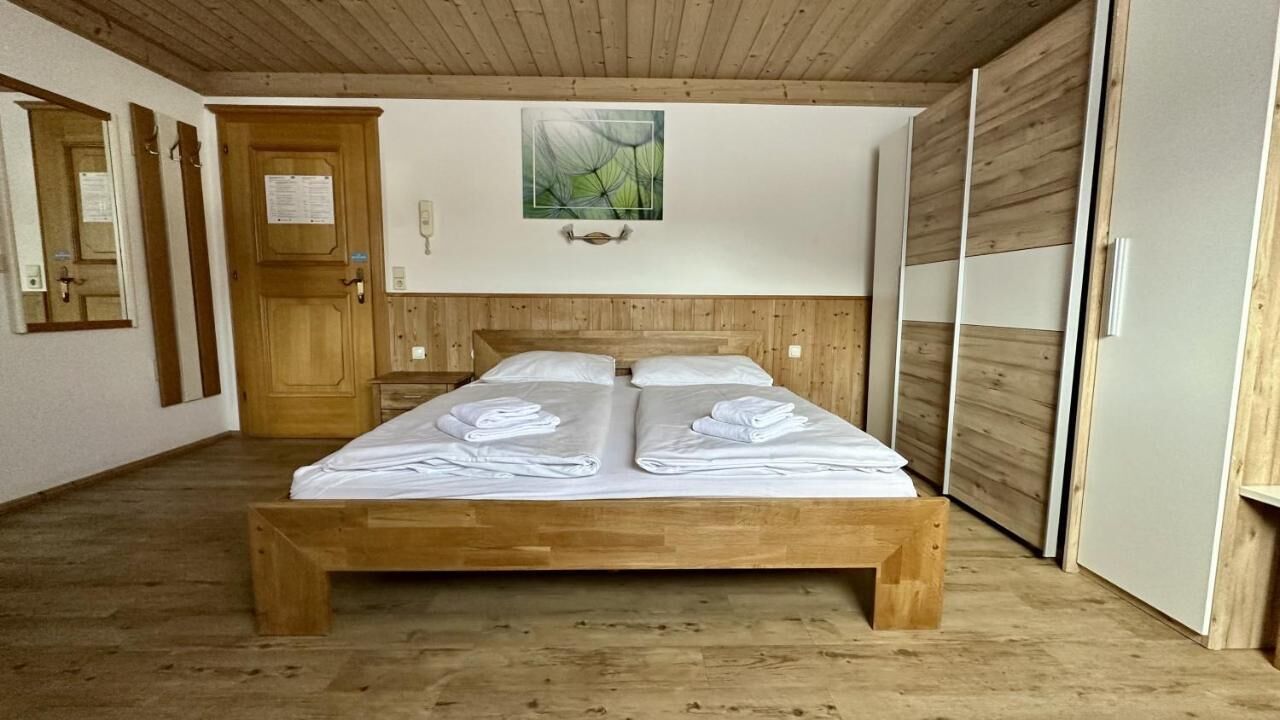 Una cama con estructura de madera y ropa de cama blanca, un armario de madera y un cuadro en la pared.