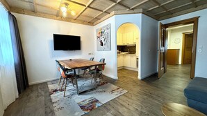 Un comedor con mesa y sillas de madera, un televisor de pantalla plana en la pared y una cocina al fondo.