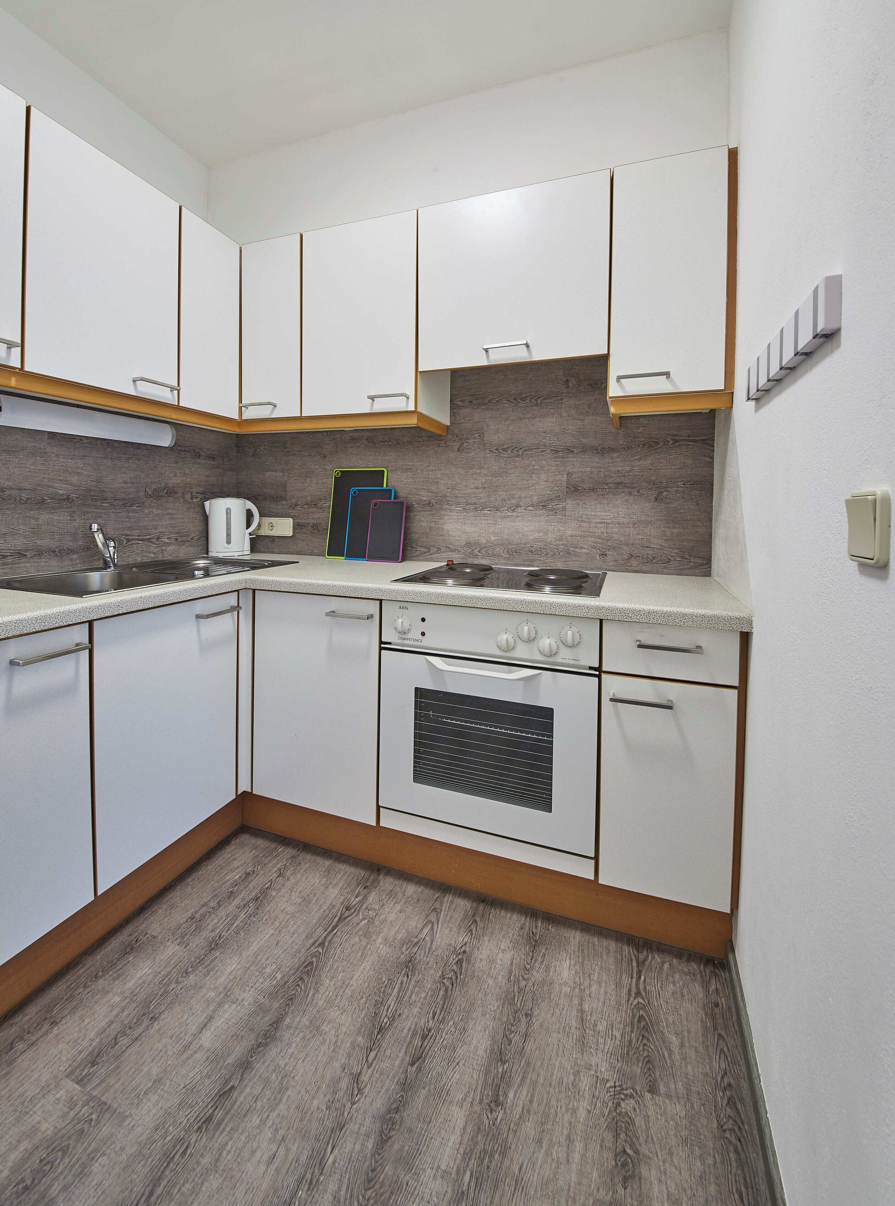 Een moderne keuken met witte kasten, een inbouwoven en een houten achterwand.