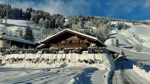 Una cabaña de madera con balcón, rodeada de árboles cubiertos de nieve y una pista de esquí.