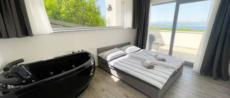 Un dormitorio moderno con una cama grande, una bañera negra y un balcón con vistas al mar.