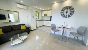 A modern living room with a glass coffee table, a sofa with yellow cushions, and a dining area with two chairs. A large wall clock is visible. - Villa Linda 2 (Crikvenica)