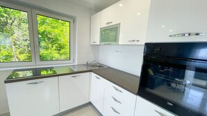 A modern kitchen with white cabinets, a black oven, and a window with a view of greenery. - Villa Linda 2 (Crikvenica)