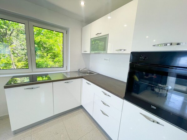 A modern kitchen with white cabinets, a black oven, and a window with a view of greenery.