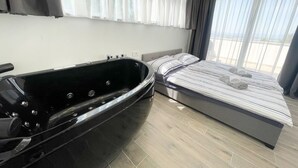 A modern bedroom with a large black bathtub, a bed with striped bedding, and a view of the outdoors through sheer curtains. - Villa Linda 2 (Crikvenica)