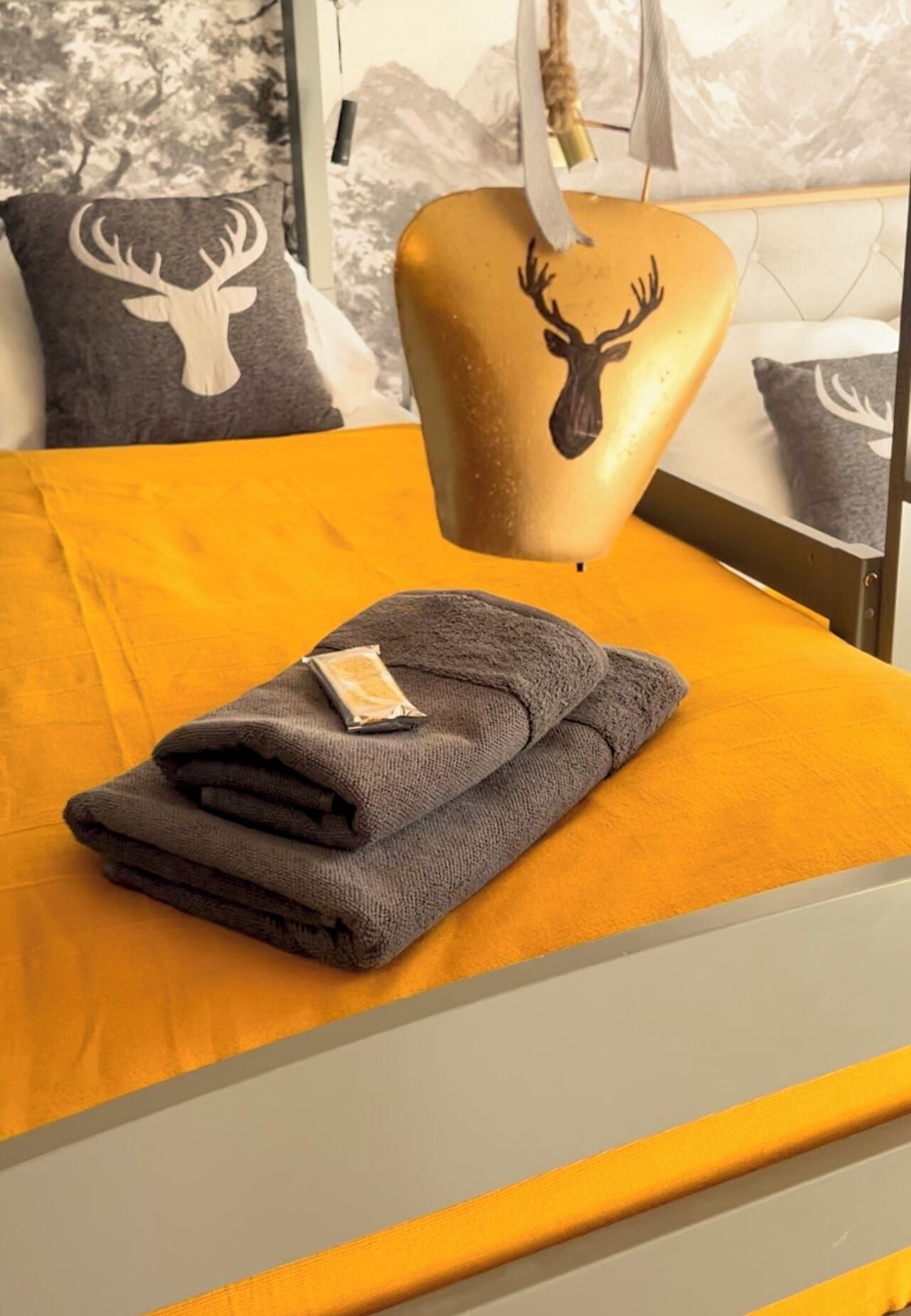 A neatly made bed with a folded gray towel and a small packet, possibly a snack, on it.