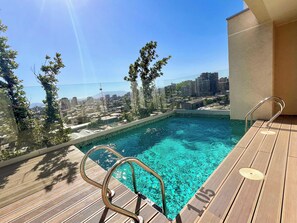 A rooftop pool with a city view, surrounded by trees and a clear sky.