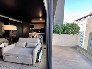 A modern living room with a sofa, a coffee table, and a dining area with a table and chairs. There is a kitchen visible in the background.
