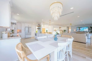 Un vaste espace de vie comprenant une table à manger, des meubles blancs, un lustre et un téléviseur.