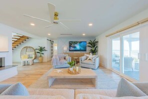 A modern living room with a flat-screen TV, a ceiling fan, and a staircase leading to an upper level.