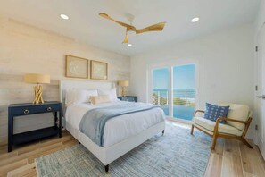 A bedroom with a bed, nightstands, a chair, a ceiling fan, and a balcony with a view.