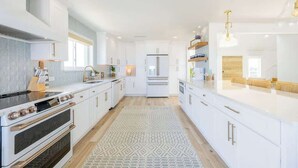 Une cuisine moderne avec des meubles blancs, un îlot central et un tapis à motifs.