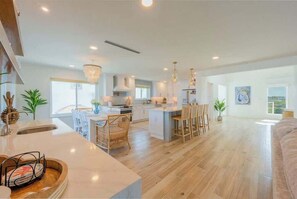 A modern kitchen with a central island, dining area with chairs, and a living room with a sofa.