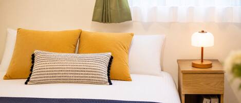 A neatly made bed with two pillows, a bedside table with a lamp, and a book on the table.