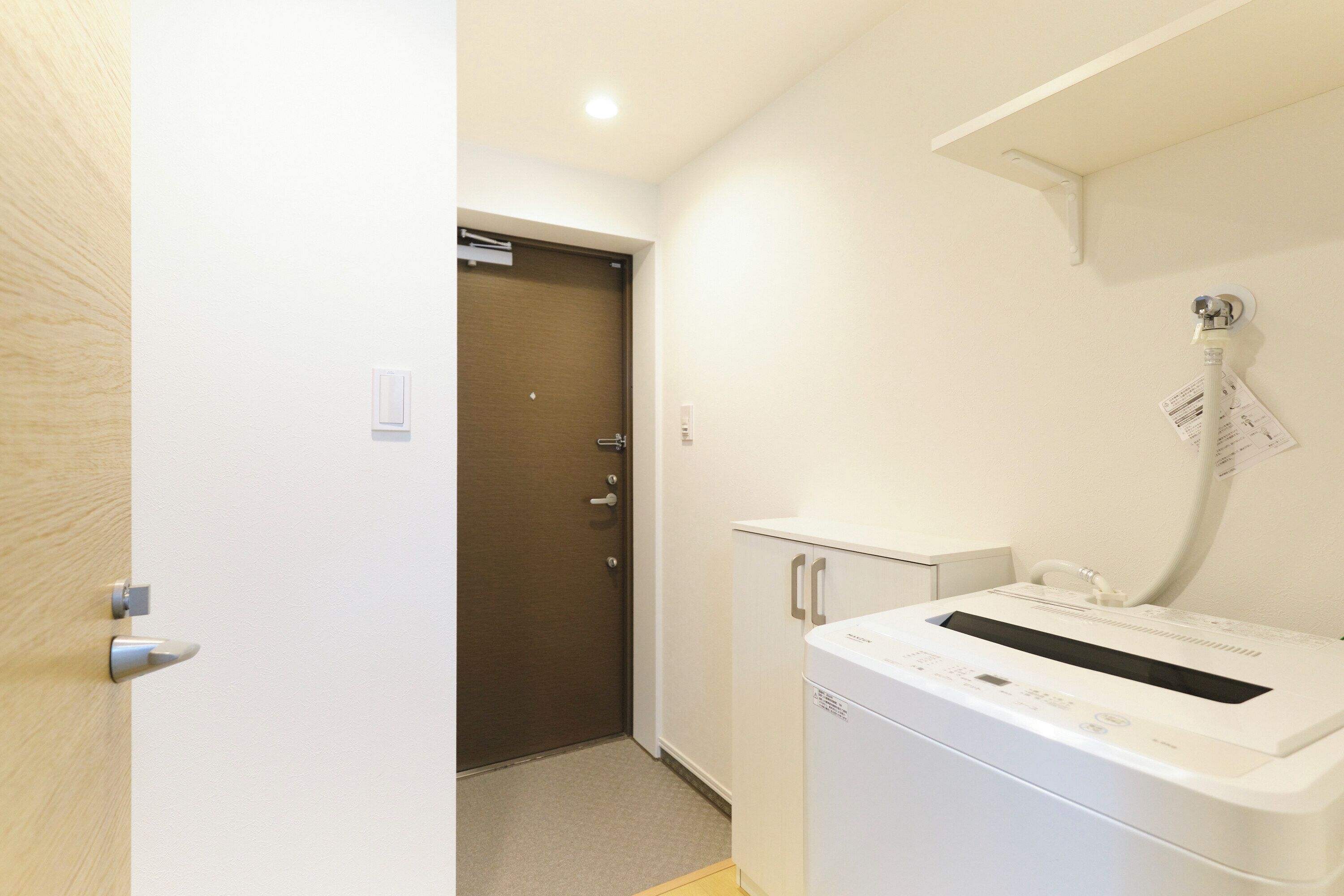 A compact hotel room with a wooden door, a white washing machine, and a small cabinet.