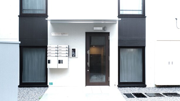 A modern building with a dark entrance door, a small window above the door, and a sign above the door.