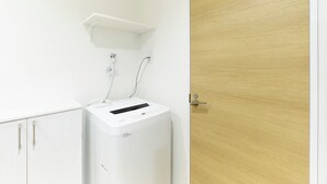 A compact room with a white washing machine, a wooden door, and a white cabinet with silver handles.