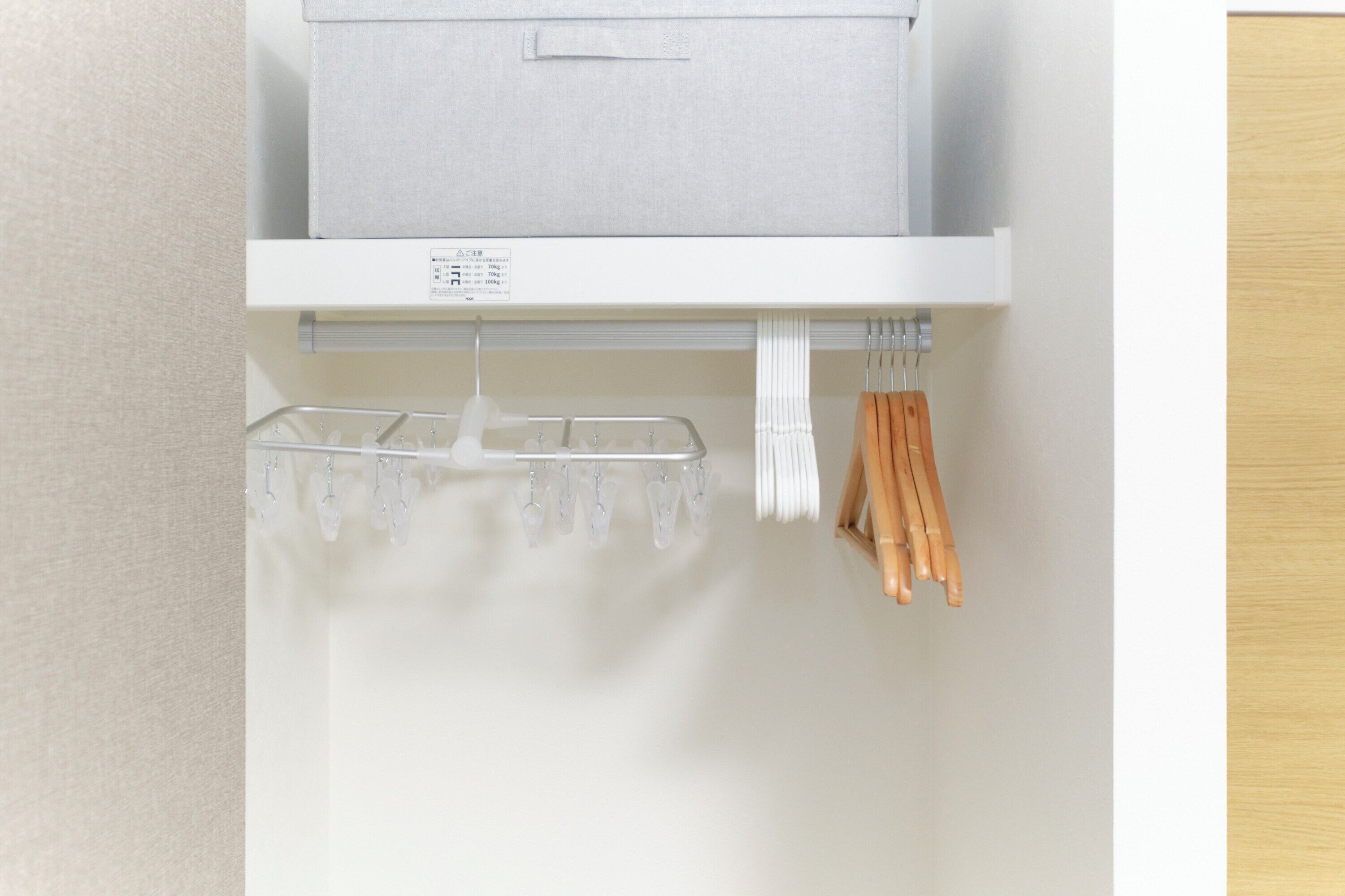 Une étagère blanche avec une boîte de rangement grise et un porte-objets suspendu contenant des articles blancs et en bois.