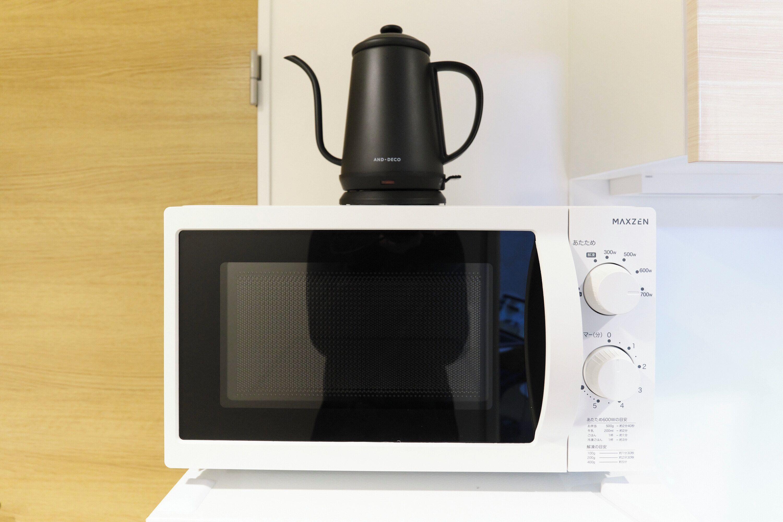 Eine weiße Mikrowelle mit einer schwarzen Kaffeemaschine darauf.