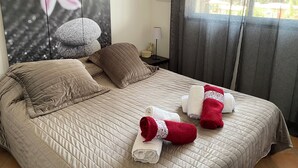 A neatly made bed with a quilted bedspread, two pillows, and two rolled towels with a red rose and white lace detail. - Waterfront apartment 2/3 pers. Porto-Vecchio (Porto-Vecchio)