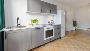 A modern kitchen with grey cabinets, a stainless steel sink, a built-in oven, and a small countertop with a plant and fruit bowl. - ShortStayPoland Waliców B171 (Warsaw)