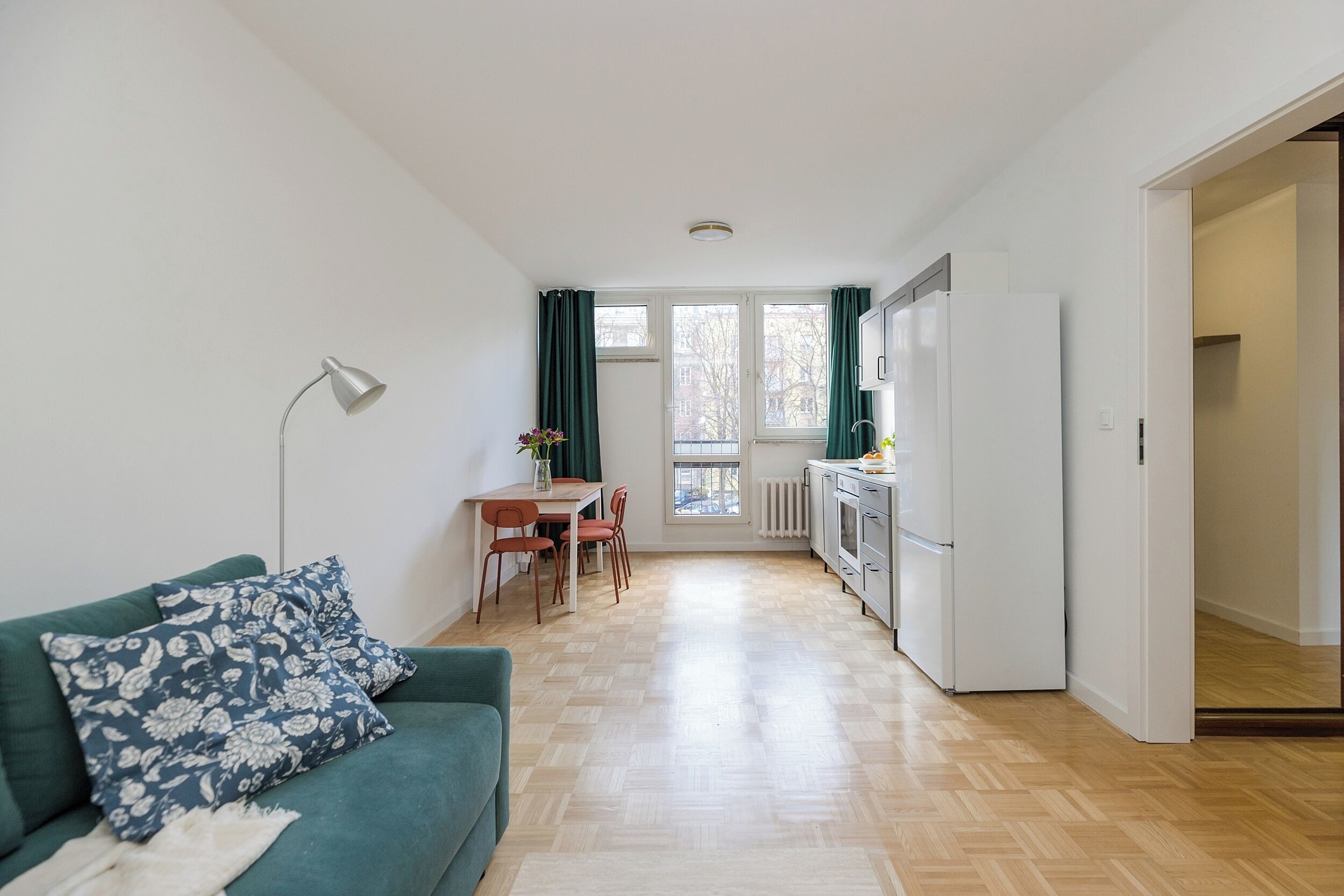 Un appartement moderne avec un canapé vert, une table à manger avec des chaises, un coin cuisine et une vue par la fenêtre.