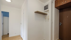 A hallway with a wooden floor, white walls, a wooden door, and a mounted telephone. - ShortStayPoland Waliców B171 (Warsaw)