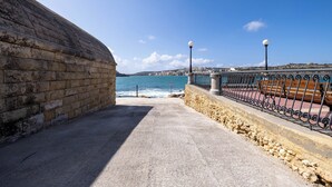A coastal walkway with a stone wall on one side and a metal railing on the other, leading to the sea. - Cozy Living 2 BR Apartment Walk to Sea (San Pawl il-Baħar)
