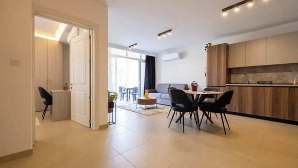 A modern kitchen with a dining area, a sofa, and a view to the outside. - Cozy Living 2 BR Apartment Walk to Sea (San Pawl il-Baħar)