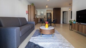 A modern living room with a grey sofa, a round coffee table with a vase, and a TV on a wooden cabinet. - Cozy Living 2 BR Apartment Walk to Sea (San Pawl il-Baħar)