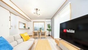 Una sala moderna con sofá, mesa de centro, televisor, mesa de comedor, sillas y una lámpara de techo.