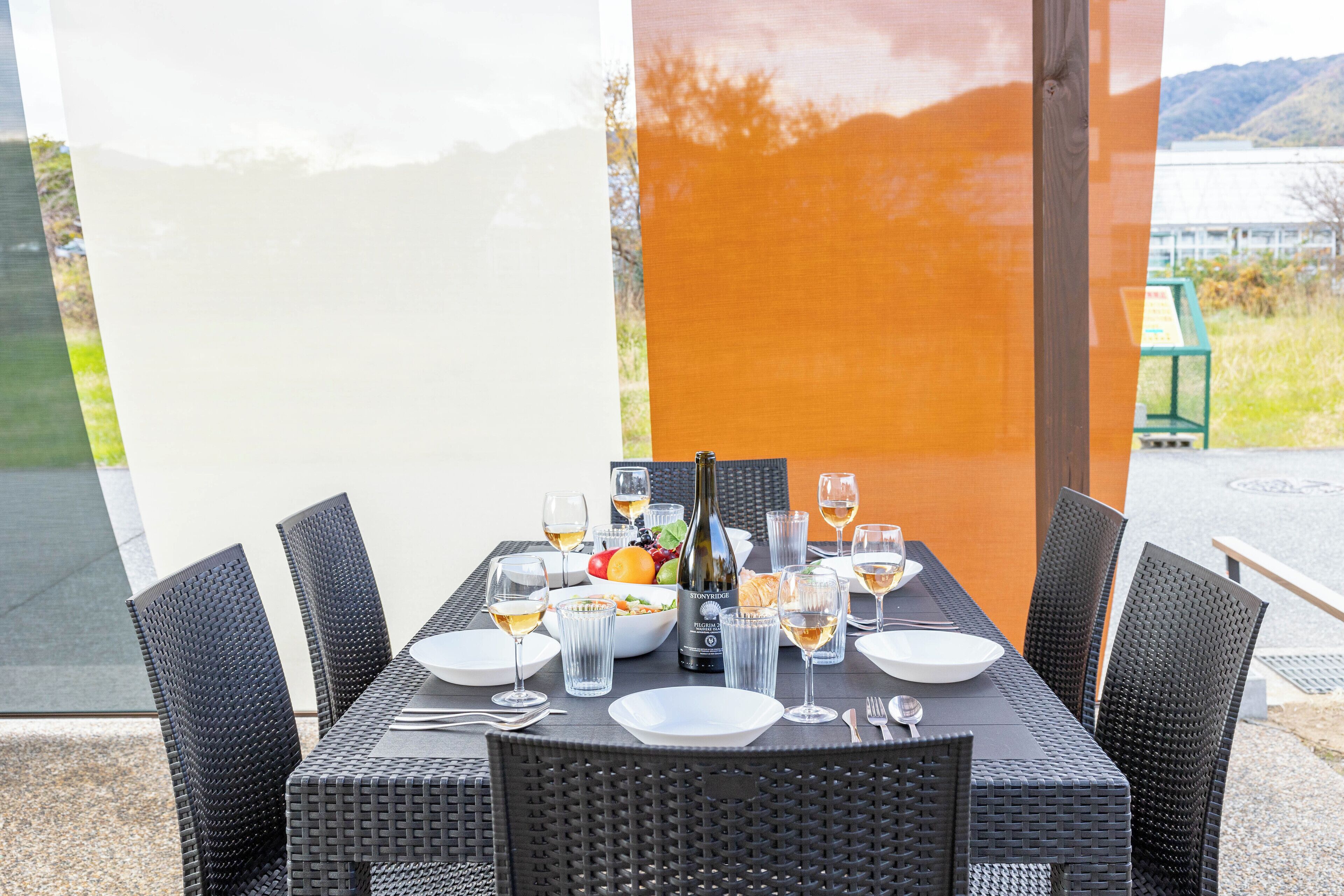 Una mesa de comedor dispuesta con platos, vasos, cubiertos, una botella y un frutero.