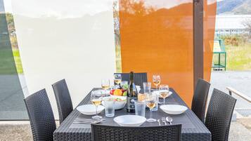 Una mesa de comedor dispuesta con platos, vasos, cubiertos, una botella y un frutero.