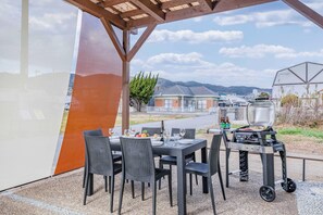 An outdoor dining area with tables and chairs, a grill, and a view of buildings and hills in the background. - Seaside House-THE BLUE- (Awaji)