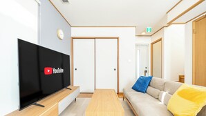 Una sala moderna con un televisor de pantalla plana, una mesa de centro de madera, un sofá con cojines y una puerta corredera.