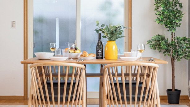 Una mesa de comedor con sillas, un florero con flores y una botella de vino.