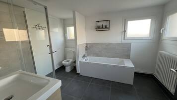 Et stilfuldt badeværelse med badekar, toilet og bruseniche.