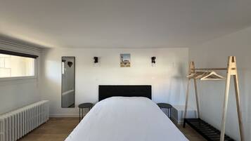 A bedroom with a large bed, a radiator, a mirror, a small table, and a wooden drying rack.