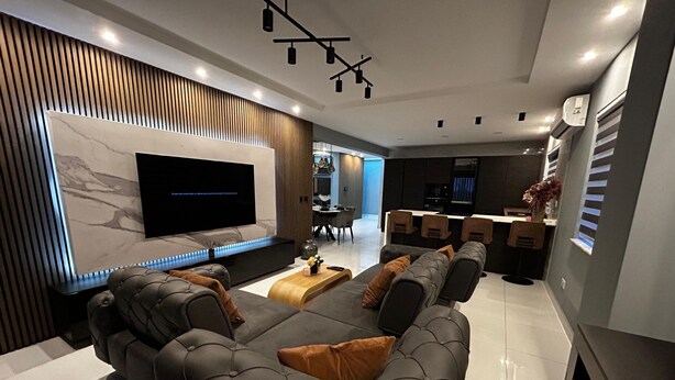 Ein modernes Wohnzimmer mit einem großen Flachbildfernseher, einem Ledersofa und einem Essbereich mit Bar.