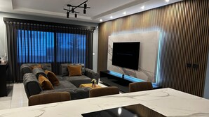 Ein modernes Wohnzimmer mit einer Couch, einem Couchtisch und einem an einer Wand mit Holzpaneelen befestigten Fernseher.