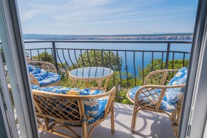 A balcony with wicker furniture and a glass table, overlooking a body of water and distant land.